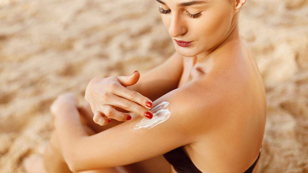 Young woman applying sunscreen at beach to repel bugs